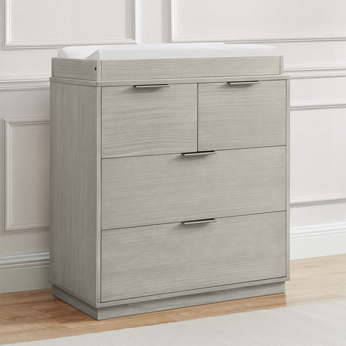 Gray dresser with three drawers in a room with white paneled walls.