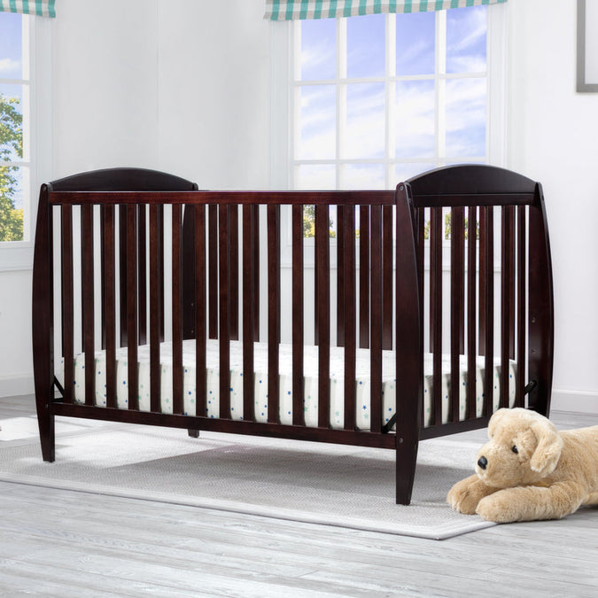 Wooden crib in a bright room with a teddy bear on the floor. 14-Taylor 4-in-1 Convertible Crib