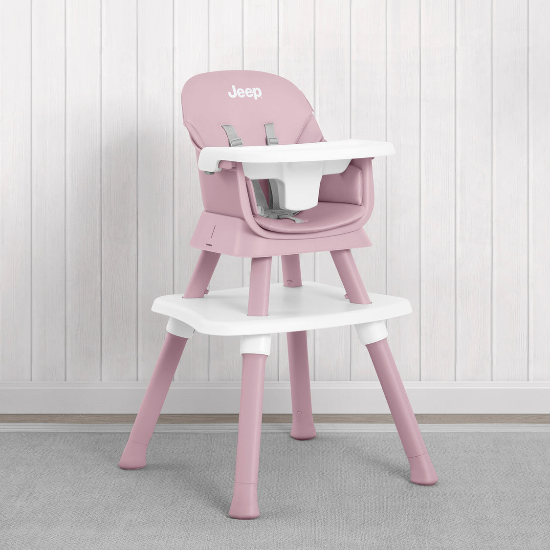 A pink and white Jeep high chair with a matching tray table, set against a white wood-paneled wall and gray carpet.