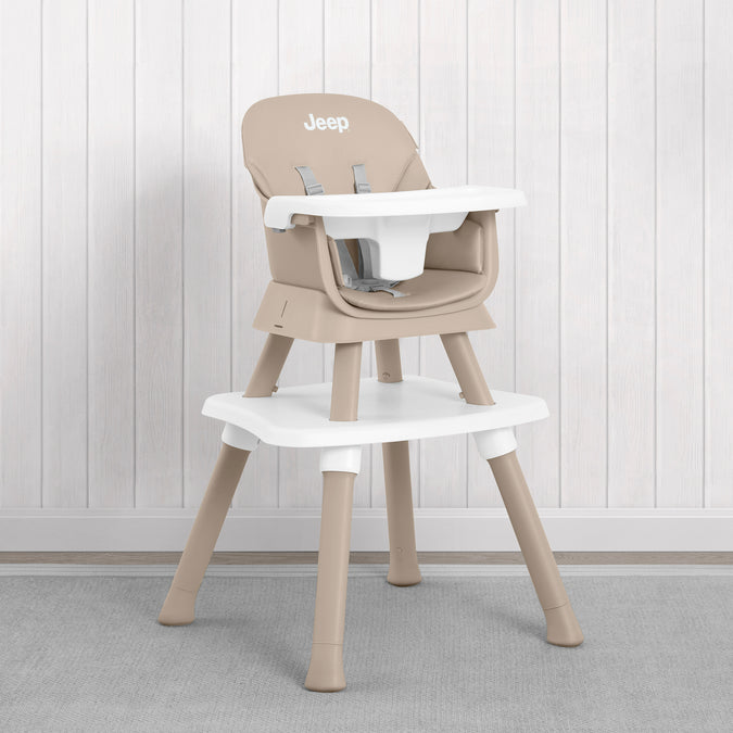 A beige and white Jeep high chair with a matching footrest, set against a white paneled wall and gray carpet. 60-Milestone 6-in-1 High Chair