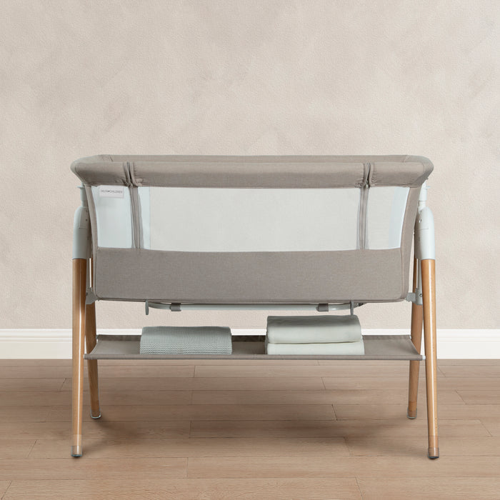 Baby crib with gray mesh and wooden legs on a wooden floor. 2-Bondi Adjustable Height Bedside Beechwood Bassinet
