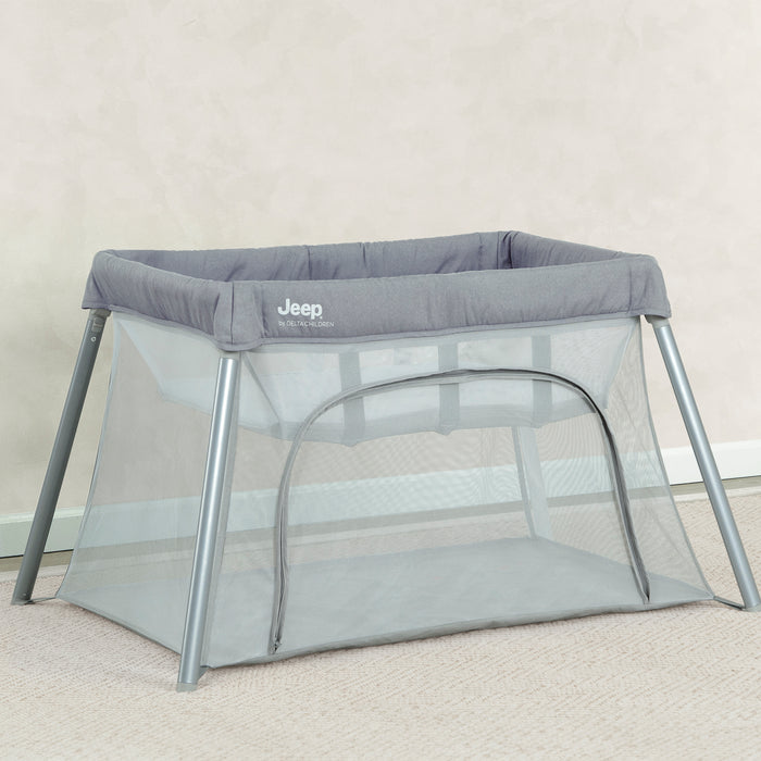 Gray portable crib with Jeep logo on a beige carpet 1-Horizon Compact Travel 2-in-1 Play Yard and Bassinet