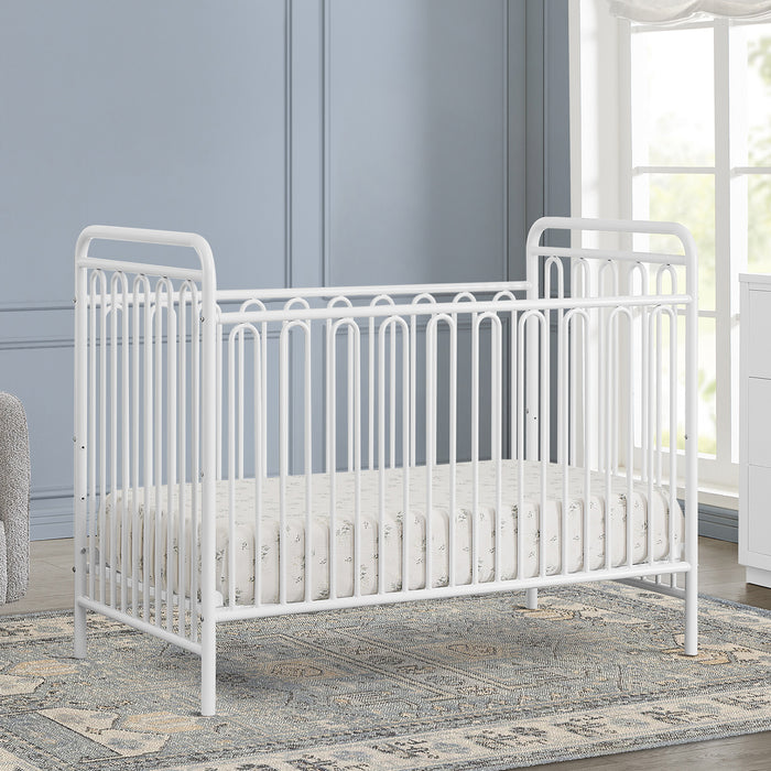 White crib in a nursery with a blue wall and window. 2-Darcy 4-in-1 Convertible Metal Crib