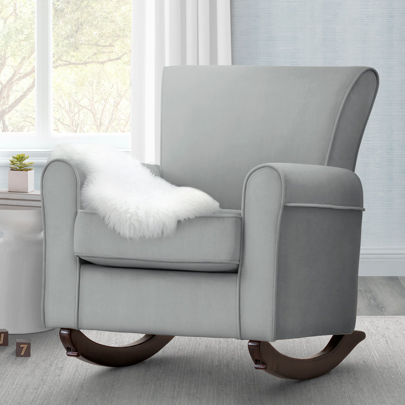 Gray rocking chair with a white pillow in a room with large windows.