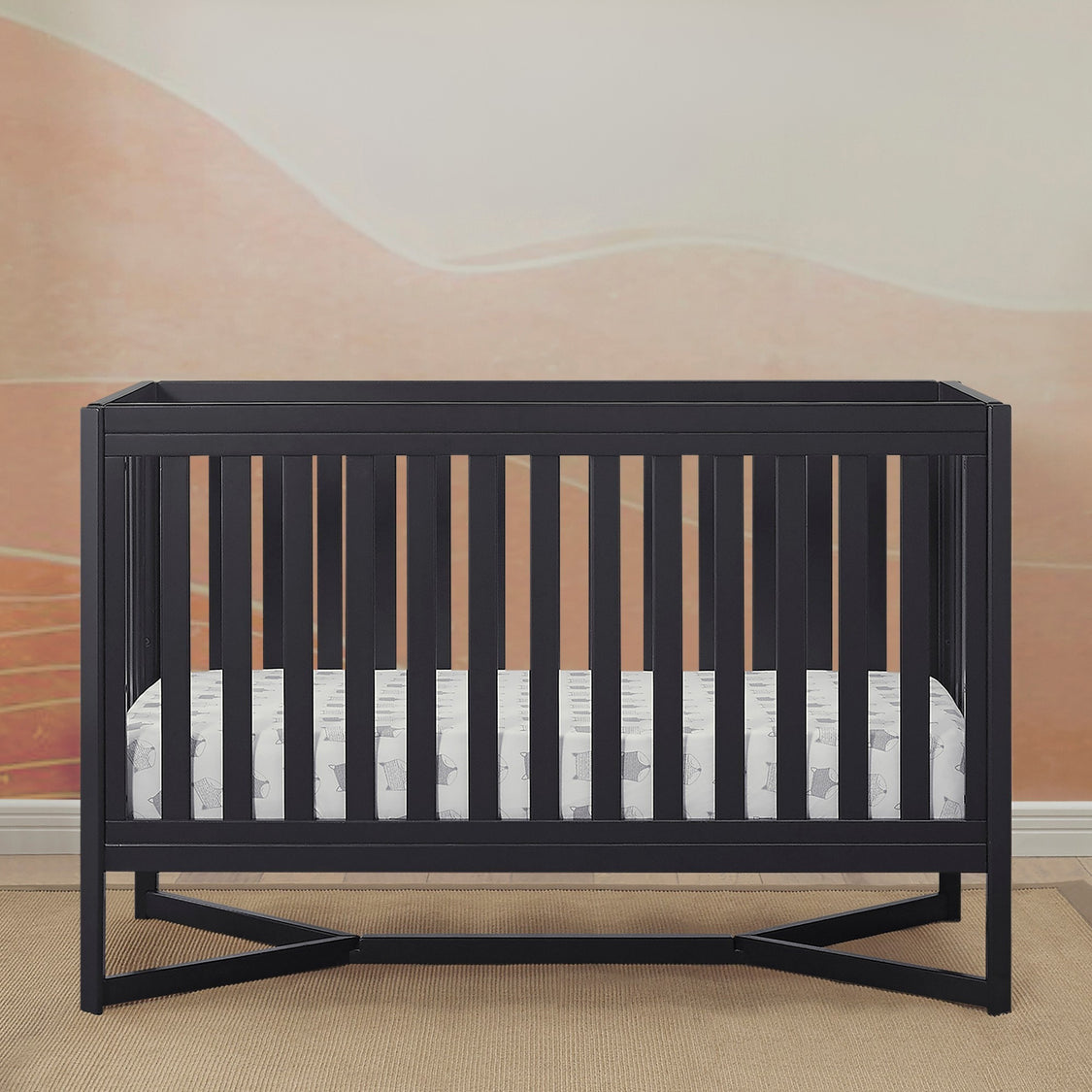 Black crib with a white mattress in a room with a pink wall.