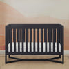 Black crib with a white mattress in a room with a pink wall. 21-Tribeca 4-in-1 Convertible Crib