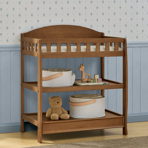 Wooden changing table with toys and baskets against a blue paneled wall.