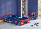 A children's bed styled with Spider-Man graphics, featuring a blue and red frame with spider web patterns and character decals. The bed is shown in a decorated bedroom with Spider-Man themed wallpaper, a matching armchair, and toy cars on the floor. 14-Spidey and His Amazing Friends Foam Frame Race Car Toddler Bed