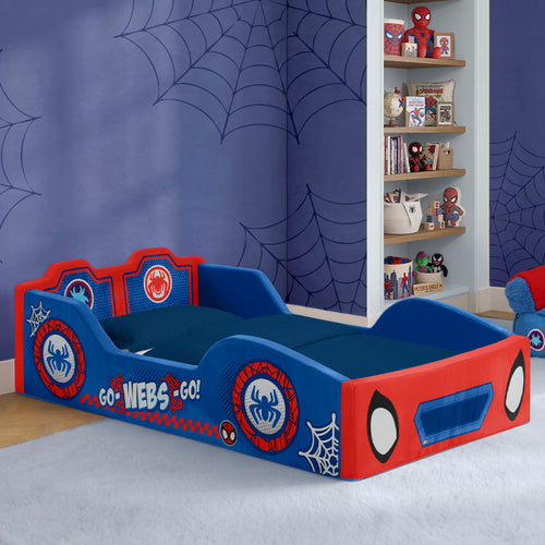 A children's Spider-Man themed single bed frame in red and blue, styled in a bedroom with blue spiderweb wallpaper and a bookshelf.