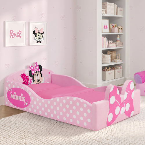 A pink Minnie Mouse children's bed with white polka dots and Minnie Mouse-themed headboard and footboard, shown in a styled children's bedroom with shelves and wall art.