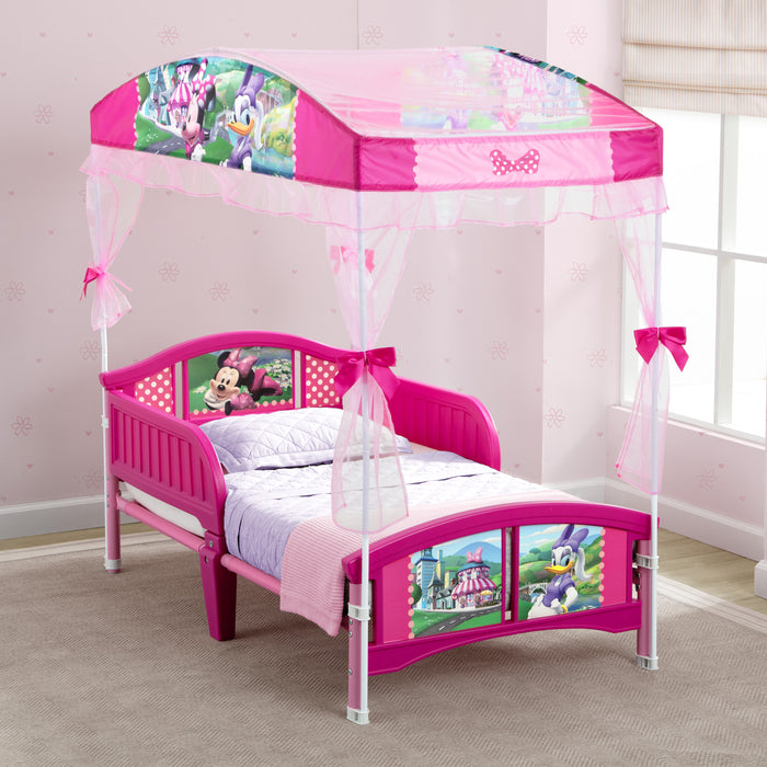 Pink children's bed with canopy featuring cartoon characters in a room. 3-Minnie Mouse Toddler Canopy Bed