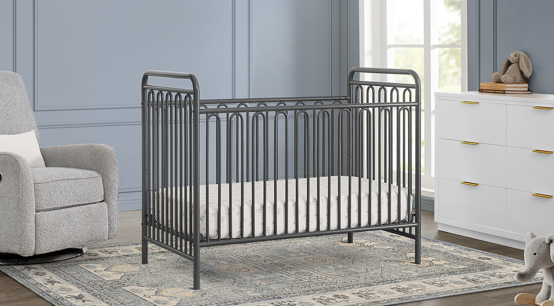 Nursery room with a metal crib, gray armchair, and white dresser.