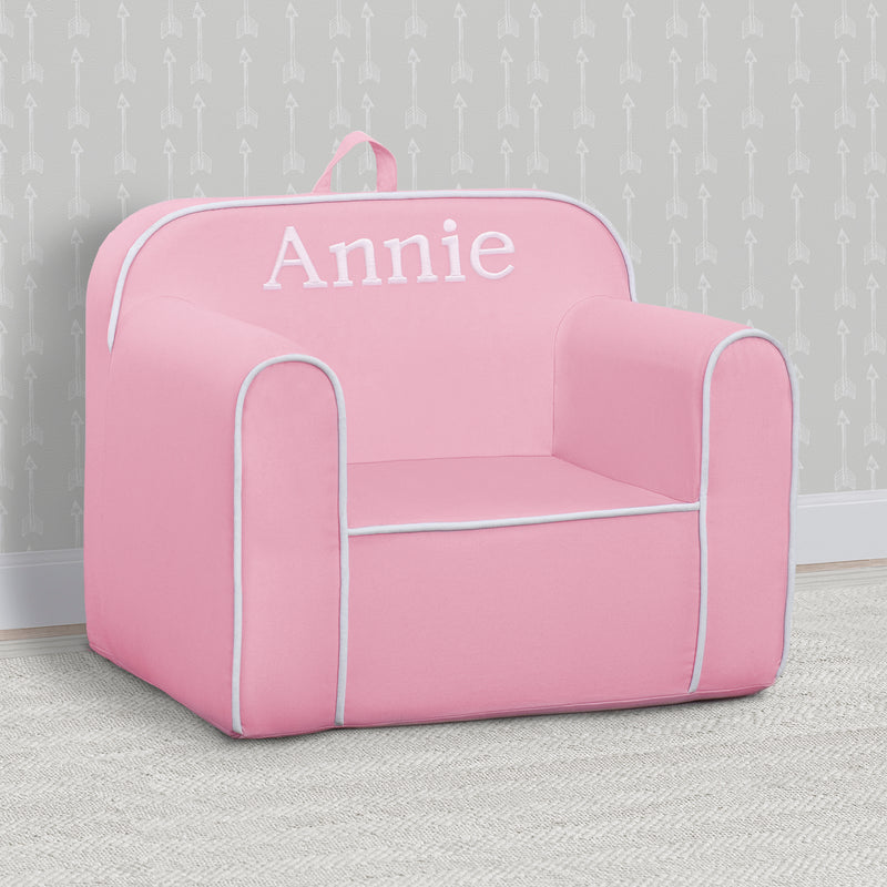 Pink children's chair with 'Annie' printed on it against a gray wall.