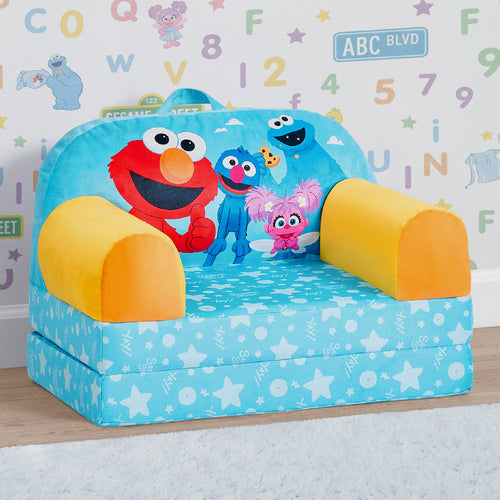 A children's fold-down play couch or small bed in a Sesame Street theme, featuring Elmo, Grover, Abby, and Cookie on a light blue star-patterned seat, with yellow armrests, set against a child's room wall with alphabet letters.