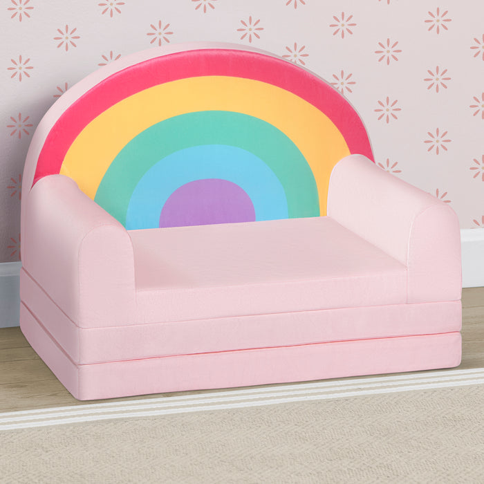 Pink children's chair with a rainbow backrest against a patterned wall. 2-Cozee Rainbow Figural Flip-Out 2-in-1 Convertible Chair to Lounger