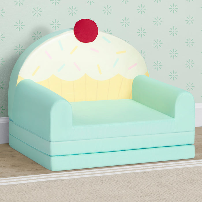 Children's chair designed like a cupcake with a cherry on top against a light green wall. 2-Cupcake Rainbow Figural Flip-Out 2-in-1 Convertible Chair to Lounger