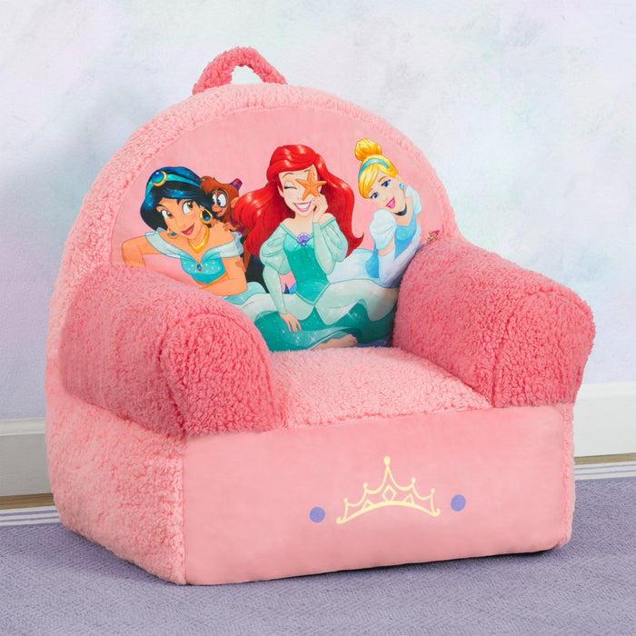A pink plush chair with Disney Princess graphics featuring Ariel, Jasmine, and Cinderella, designed for kids' rooms. 1-Disney Princess Cozee Buddy Chair