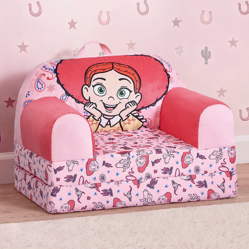 A small pink children's armchair with a cartoon cowgirl graphic on the backrest and a matching printed cushion, photographed in a styled room setting with a patterned pink wall and wood floor.