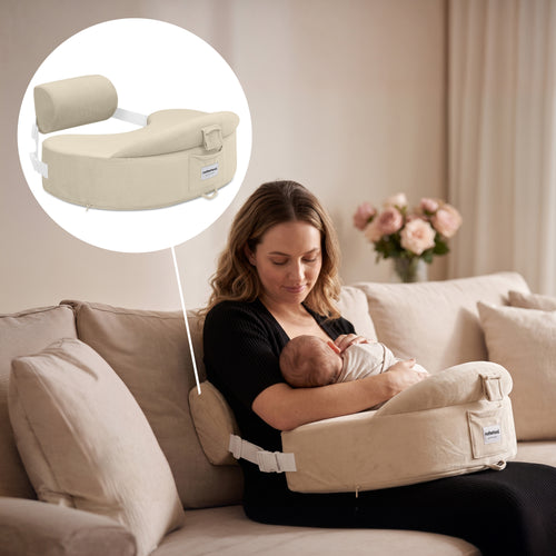 A woman in a black top sits on a beige sofa holding a baby in a beige nursing pillow support. A circular inset at the top left shows a close-up of the beige nursing pillow with a small blue brand tag.
