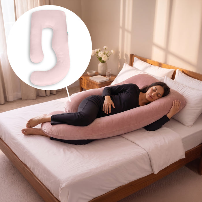 A woman lies on a bed using a large pink U-shaped maternity pillow, with a circular inset showing a close-up of the pillow's shape. The room has warm sunlight, white bedding, and a wooden headboard. 1-U-Shaped Pregnancy Pillow