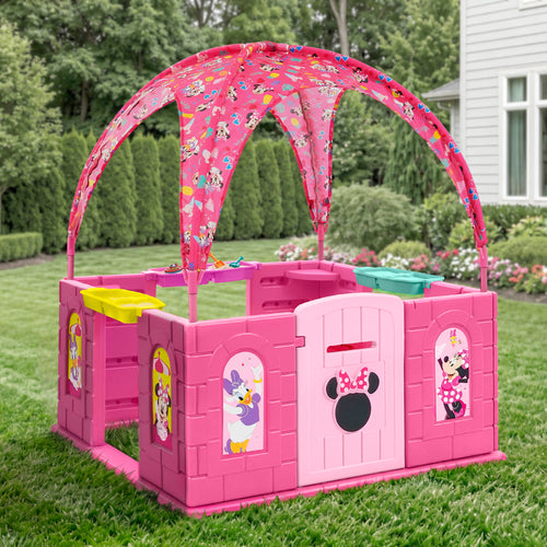 Pink plastic children's playpen with a matching arched canopy featuring cartoon Minnie Mouse prints, set on a green lawn in front of a house.
