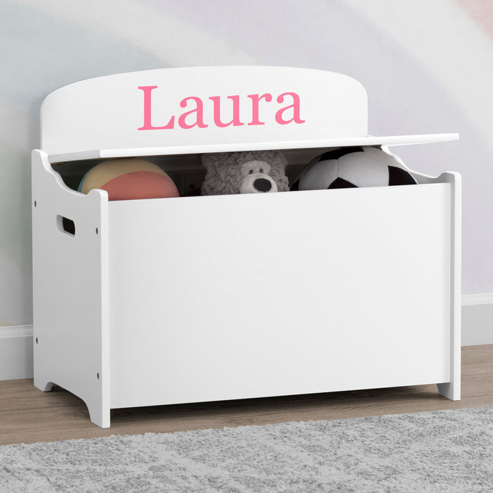 White toy storage box with 'Laura' on top, containing toys, against a light gray wall. 1-Personalized MySize Deluxe Toy Box