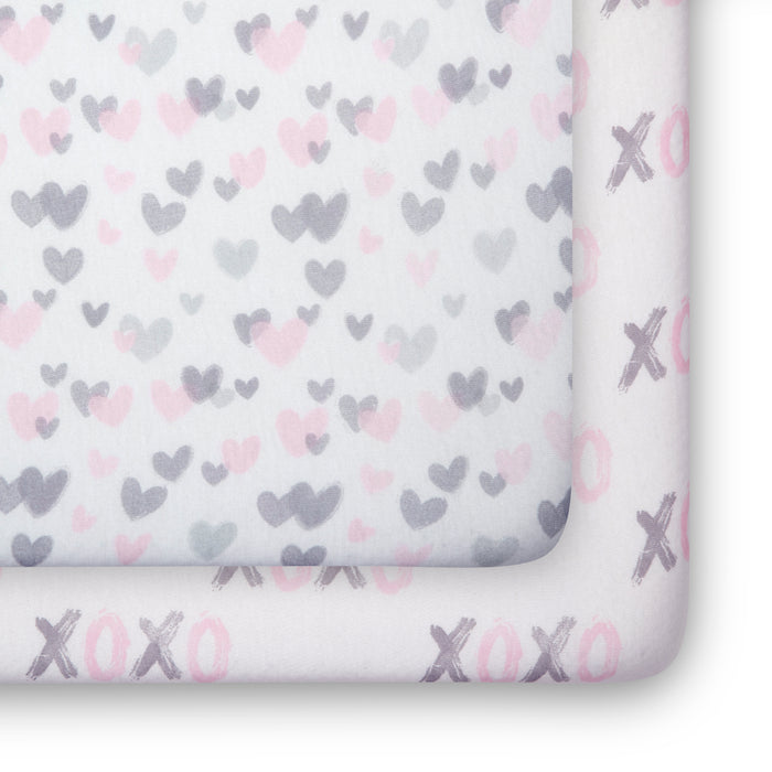 Two folded crib sheets with heart and xoxo patterns on a window sill. 0-Hearts N Kisses Fitted Crib Sheets - 2 Pack