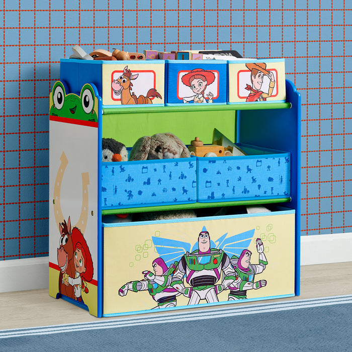 A children's toy storage organizer with colorful cartoon graphics, including Buzz Lightyear on the front drawer and Toy Story characters on the top panels. The unit has three tiers with open shelves and blue fabric bins, shown filled with toys against a blue patterned wallpaper background. 3-Toy Story 6 Bin Design and Store Toy Organizer
