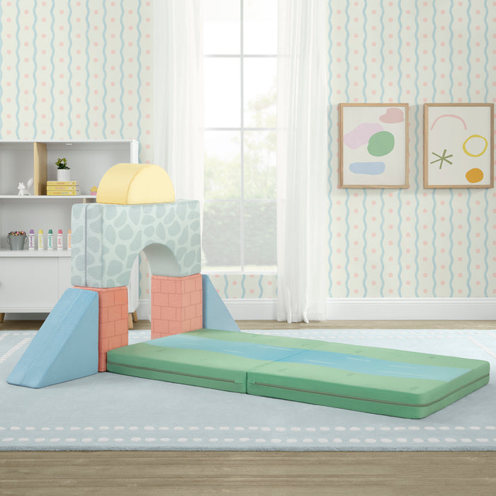 Children's play area with a green mat, slide, and tunnel in a room with colorful walls and decor. 1-7-Piece Foam Fortress