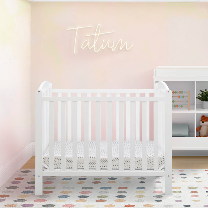 White crib in a nursery with a polka dot rug and a neon sign on the wall. 1-Sprout Mini Crib with Mattress