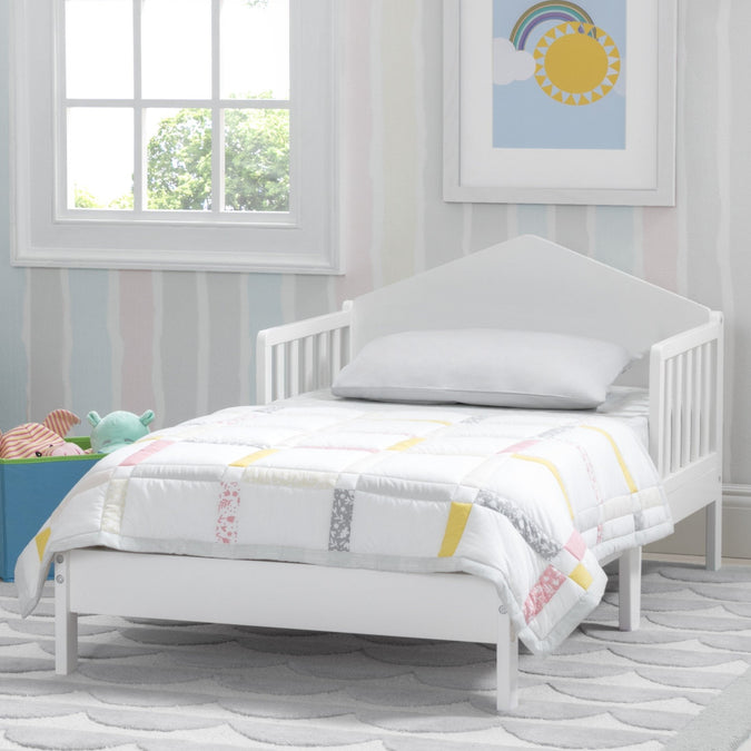 White children's bed with colorful bedding in a room with a window and wall art. 7-Homestead Toddler Bed