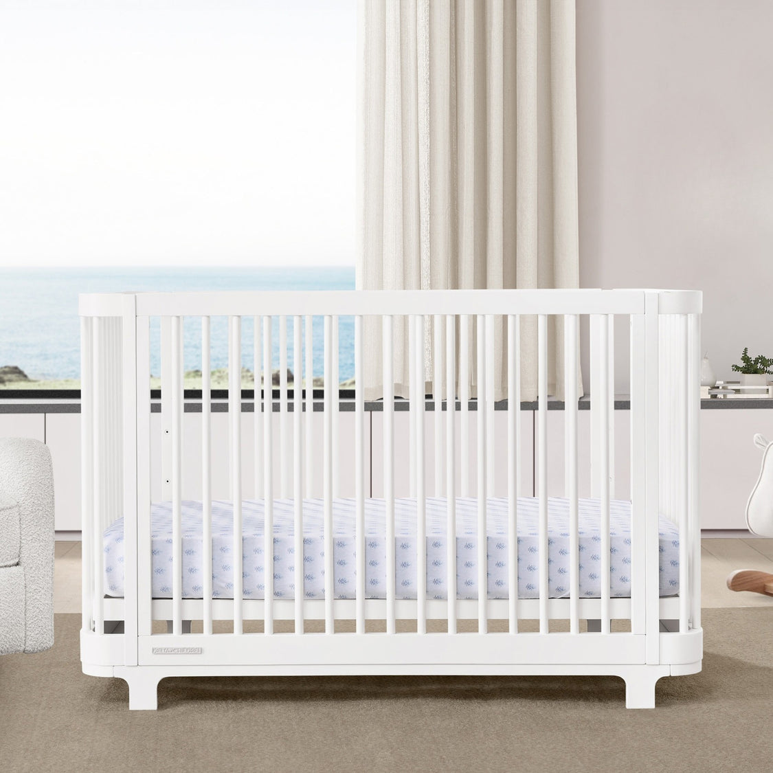 White crib in a room with curtains and a couch.