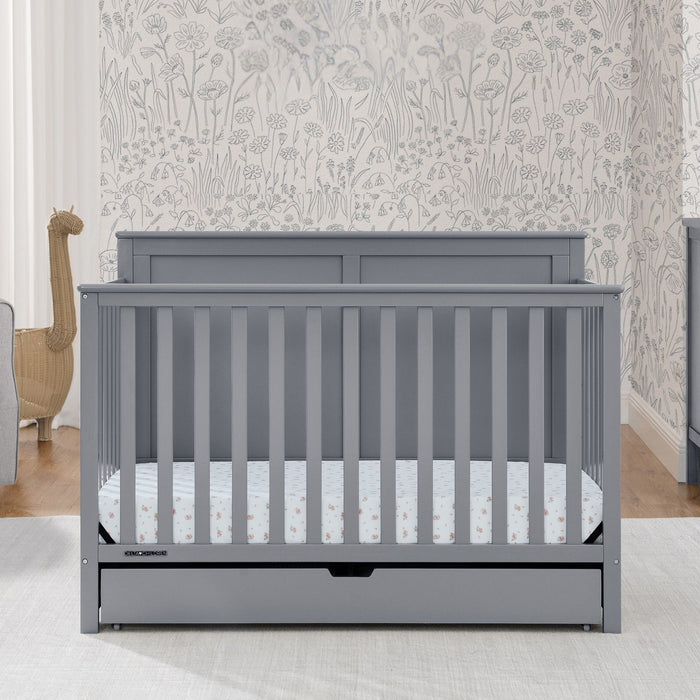 Gray crib with white mattress in a room with floral wallpaper 1-Logan 6-in-1 Convertible Crib with Underdrawer