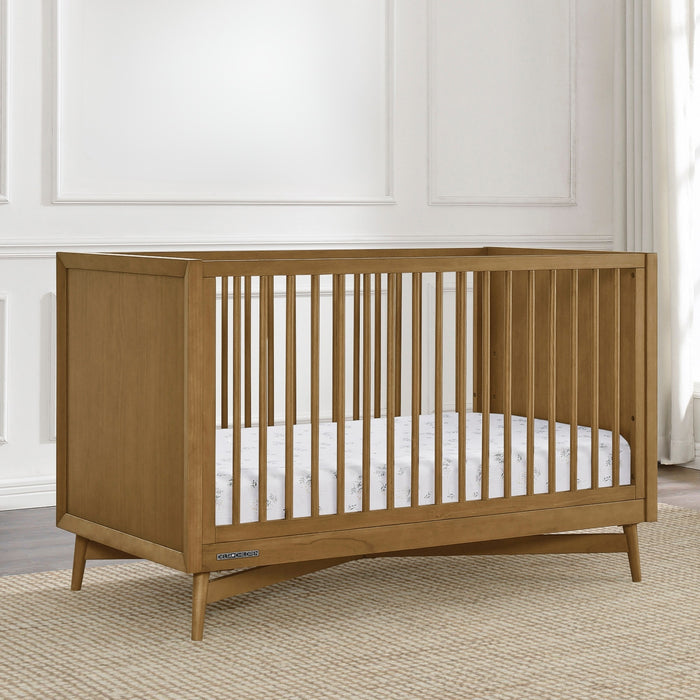 Wooden crib with white mattress in a room with white walls and a rug. 1-Dylan 4-in-1 Convertible Crib