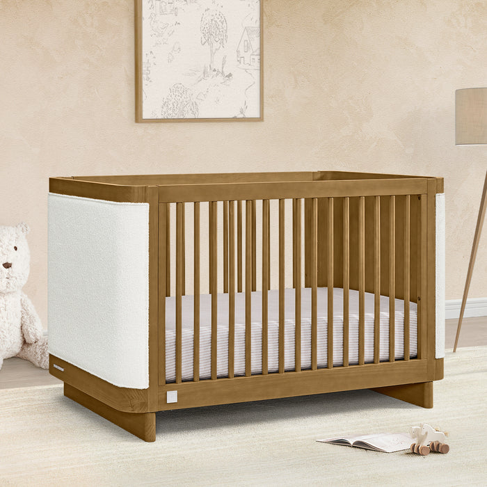 Wooden crib in a nursery with a teddy bear and lamp in the background 2-babyGap Callie 4-in-1 Upholstered Crib