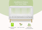 A white wooden baby crib with a white mattress featuring black polka dots, shown against a light green and white background with text reading 'Healthiest Choice For Your Baby' and certification badges below. 16-Poppy 4-in-1 Convertible Crib