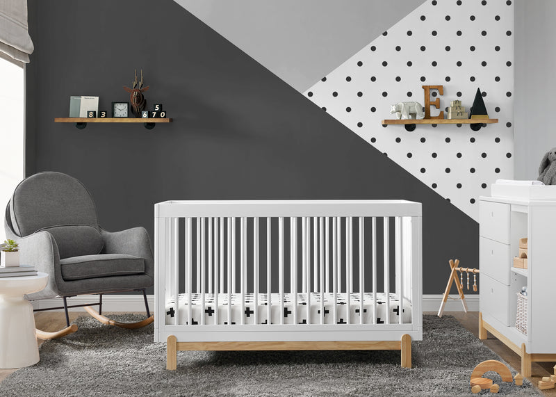 Nursery room with a white crib, gray armchair, and geometric wall design. 21-Poppy 4-in-1 Convertible Crib