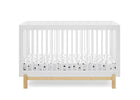 A white wooden convertible crib with a natural oak base and a white mattress featuring a black polka dot pattern, shown against a solid white background. 11-Poppy 4-in-1 Convertible Crib