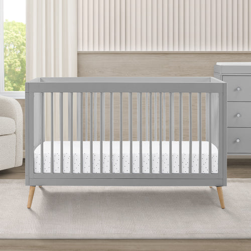 Gray crib in a nursery with a white mattress and light-colored walls.