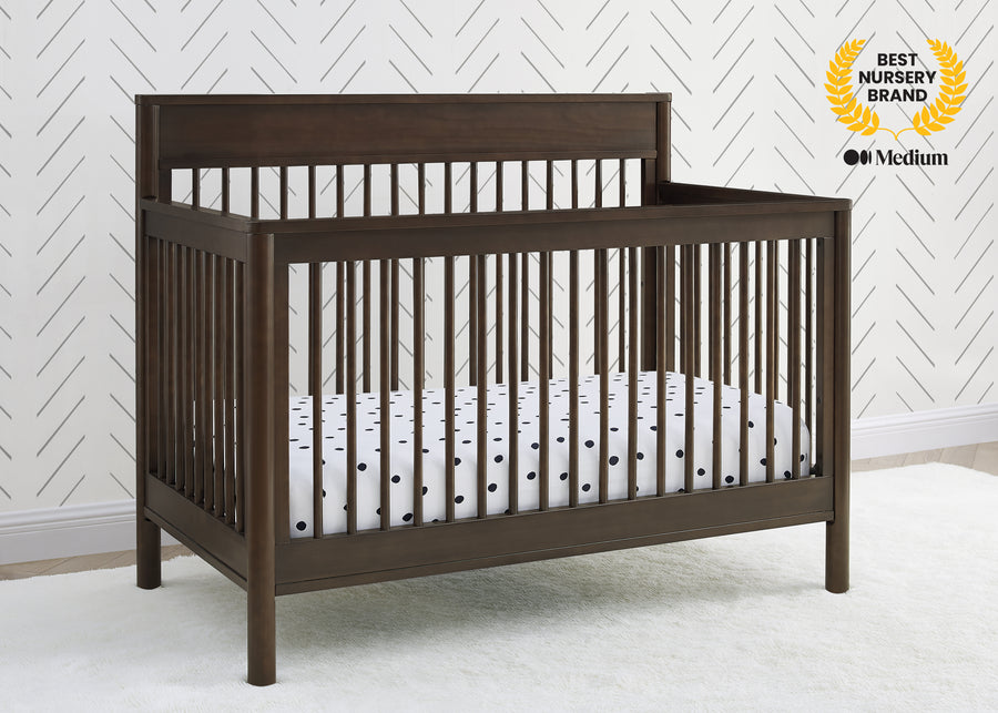 Wooden crib with white crib sheet against a white wall with a geometric pattern 24-Remy 6-in-1 Convertible Crib
