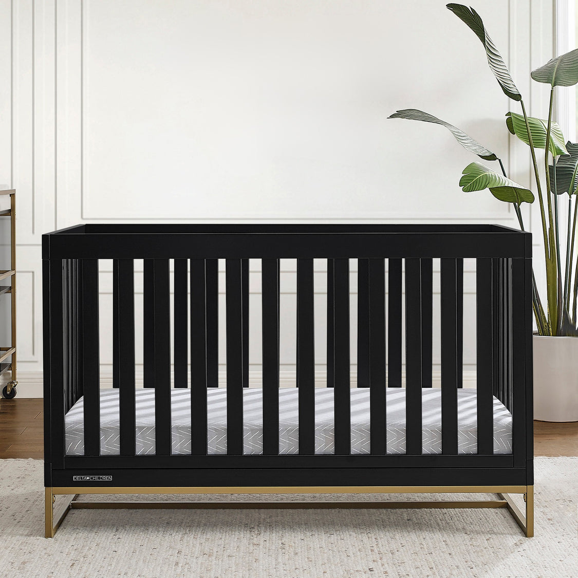 Black crib in a room with 'River Grace' wall art and plants.