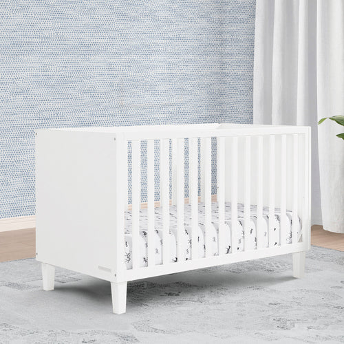 White crib in a room with textured wall and curtains