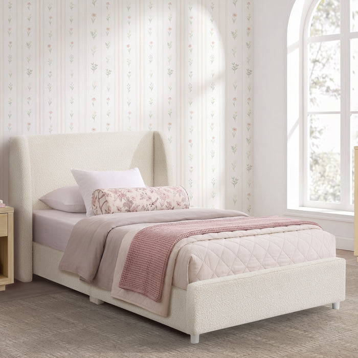 A single bed with a tall upholstered headboard and matching footboard, styled with white and blush pink bedding in a bright bedroom with floral wallpaper and a window. 0-Olivia Upholstered Twin Bed