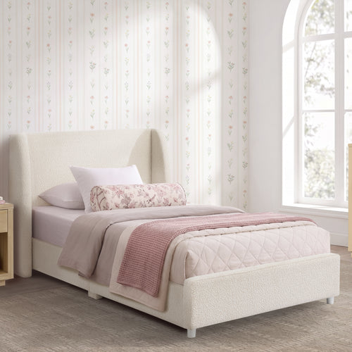A single bed with a tall upholstered headboard and matching footboard, styled with white and blush pink bedding in a bright bedroom with floral wallpaper and a window.