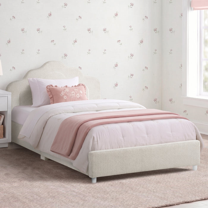 A single bed with a light beige upholstered frame, dressed in white bedding and a dusty pink throw blanket, set in a child's bedroom with floral wallpaper and a window. 2-Margot Upholstered Twin Bed
