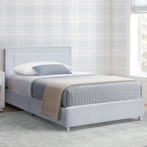 A light gray upholstered bed frame with a padded headboard and textured base, shown in a styled bedroom setting with white bedding, a blue-gray pillow, and a beige throw blanket against a plaid wallpaper background.