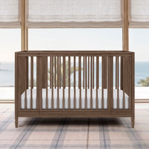 Wooden crib with white mattress in a room with large windows and plaid rug