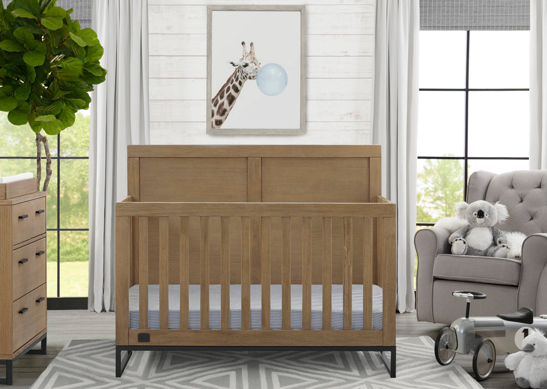 Wooden crib in a nursery with a giraffe painting on the wall and a gray chair with stuffed animals.