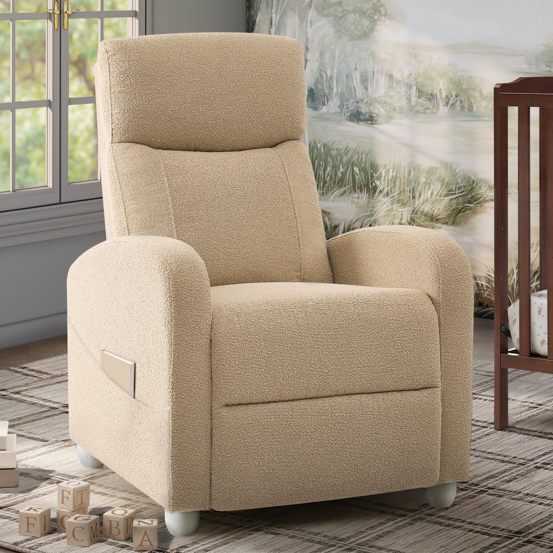 A beige upholstered recliner chair with rounded arms, a high back, and white feet, shown in a styled room setting with a window, rug, wall art, and crib visible.