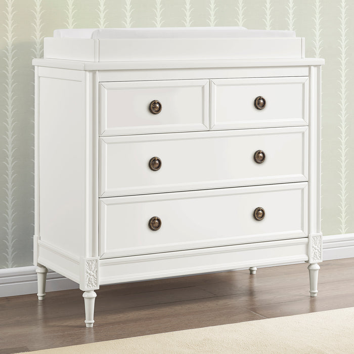 White dresser with four drawers and bronze knobs in a room with patterned wallpaper. 0-Heritage 4 Drawer Dresser with Changing Top and Interlocking Drawers